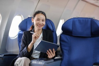 Bir kadın elinde tabletle bir uçakta oturuyor. Gülümsüyor ve uçuşun tadını çıkarıyor.