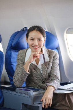 Uçakta yüzünde bir gülümsemeyle bir kadın oturuyor. Elinde bir kredi kartı tutuyor.