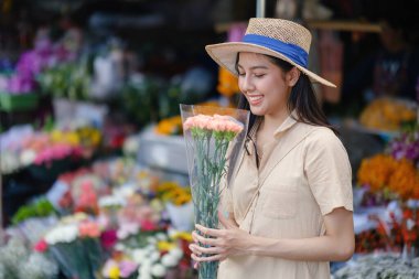 Bir kadın elinde bir buket çiçekle hasır şapka takıyor. Gülümsüyor ve eğleniyor. Çiçekler temiz bir vazoda, ve sahne bir markette ya da çiçekçide geçiyor.
