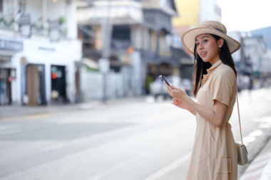 Şapkalı bir kadın elinde cep telefonu olan bir caddede duruyor. Telefona bakıyor ve acelesi var.