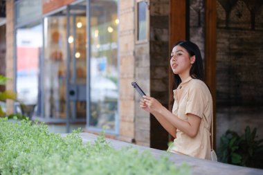 Bir kadın binanın önünde duruyor, elinde bir tablet tutuyordu. Ekrana bakıyor, muhtemelen e-postalarını kontrol ediyor ya da internette geziniyor.