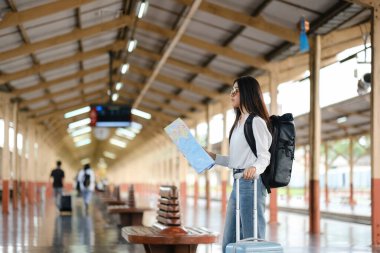 Tren istasyonunda elinde bir haritayla bir kadın duruyor. O bir sırt çantası takıyor ve yanında bir bavul var. Sahne insanlarla ve bavullarla dolu ve kadın haritasına odaklanmış durumda.