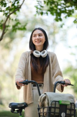 Arkasında sepet olan bir kadın bisiklete biniyor. Kulaklık ve kahverengi bir kazak giyiyor.