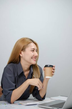 Bir kadın elinde dizüstü bilgisayar ve bir fincan kahveyle masada oturuyor. Gülümsüyor ve kahvesinin tadını çıkarıyor.