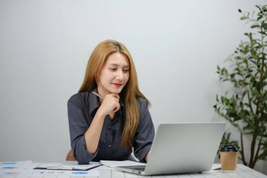 Önünde dizüstü bilgisayar olan bir kadın masada oturuyor. O, siyah bir gömlek ve bir kolye giyiyor. Laptop açık ve o ona bakıyor.