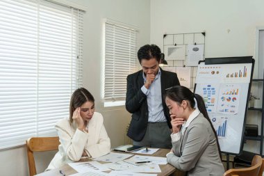 Üç kişi önlerinde kağıtlarla bir masada oturuyorlar. İçlerinden biri suratında somurtkan bir ifadeyle gazetelere bakıyor. Diğer iki kişi ona bakıyor.