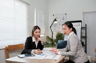 İki kadın bir odada bir masada oturmuş bir şey tartışıyorlar. İçlerinden biri bir kalem ve bir kağıt parçası tutuyor.
