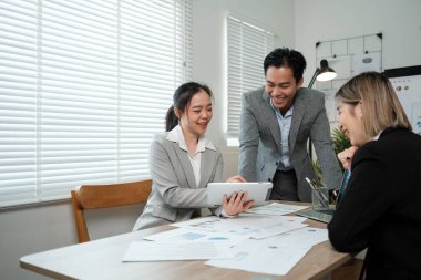 Önlerinde bir tabletle bir masada üç kişi oturuyor. Gülümsüyorlar ve iyi vakit geçiriyor gibi görünüyorlar.