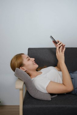 Bir kadın kanepede uzanıyor ve telefonuna bakıyor. Gülümsüyor ve eğleniyor.