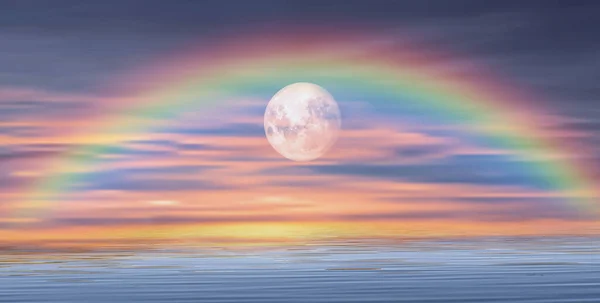 Amazing rainbow and full moon over the ocean at sunset