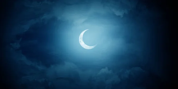 Crescent moon among the clouds in the midnight sky.