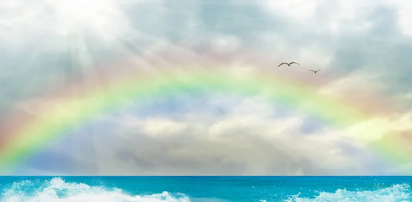 Turquoise color sea and ocean view. Sun rays among clouds and amazing rainbow in the sky.