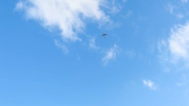 Mavi gökyüzündeki bulutlar arasında yüksek irtifada uçan sivil yolcu uçağının alttaki görüntüsü.