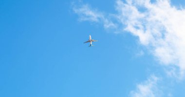 Mavi gökyüzünde bulutların arasında yüksek irtifada uçan yolcu uçağının alt görüntüsü.