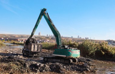 Excavator and truck clearing mud and dirt from a river after flooding clipart