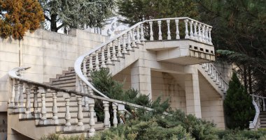Eski bir binanın bahçesindeki ağaçların arasındaki sarmal merdivenlerin dış görünüşü..