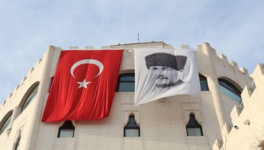 Yüksek bir kale duvarında asılı Türk bayrağı ve Atatürk portresi.
