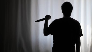 Karanlıkta beyaz bir perdenin önünde bıçak tutan bir kişinin gölgesi. Suç mahalli, cinayet, seri katil konsepti fotoğrafı..