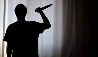 Karanlıkta beyaz bir perdenin önünde bıçak tutan bir kişinin gölgesi. Suç mahalli, cinayet, seri katil konsepti fotoğrafı..