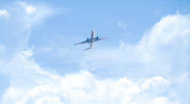 Mavi gökyüzünde kabarık beyaz bulutların üzerinde uçan yolcu uçağının ön görüntüsü.