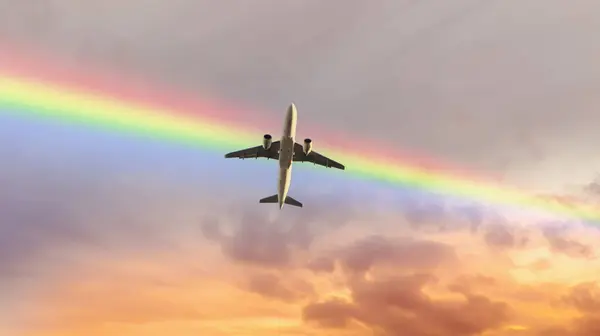 Gün batımında gökkuşağının altında uçan yolcu uçağının alt görüntüsü. Havacılık, ulaşım, tatil ve seyahat kavramı arkaplan resmi.