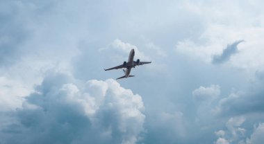 Gökyüzünde uçan yolcu uçağı ve büyük kabarık bulutlar.