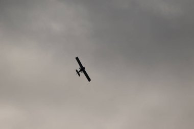 Gökyüzünde kara bulutlara karşı uçan küçük bir uçak.