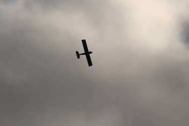 Gökyüzünde kara bulutlara karşı uçan küçük bir uçak.