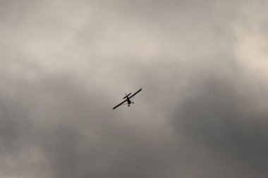 Gökyüzünde kara bulutlara karşı uçan küçük bir uçak.
