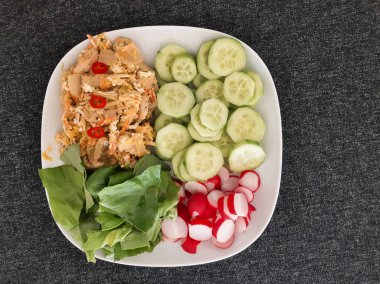 Beyaz tabakta servis edilen ev yapımı ızgara tavuk, pilav ve kimchi, yeşil salata, salatalık ve turp.