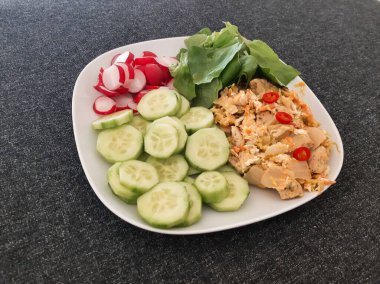 Beyaz tabakta servis edilen ev yapımı ızgara tavuk, pilav ve kimchi, yeşil salata, salatalık ve turp.