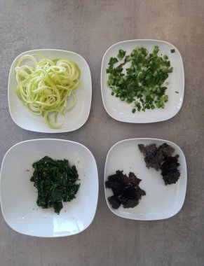 Beyaz tabakta servis edilen ıspanak, kabak sarmalı, taze soğanlı ve doğranmış nori yosunlu ev yapımı meze.