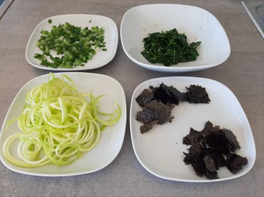 Beyaz tabakta servis edilen ıspanak, kabak sarmalı, taze soğanlı ve doğranmış nori yosunlu ev yapımı meze.