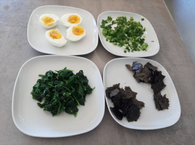 Beyaz tabakta servis edilen ev yapımı ıspanak, kabak sarmalı, taze soğan, haşlanmış yumurta ve doğranmış nori yosunlu meze.