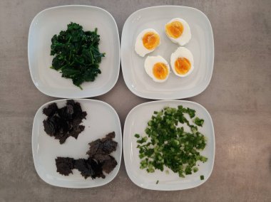 Beyaz tabakta servis edilen ev yapımı ıspanak, kabak sarmalı, taze soğan, haşlanmış yumurta ve doğranmış nori yosunlu meze.