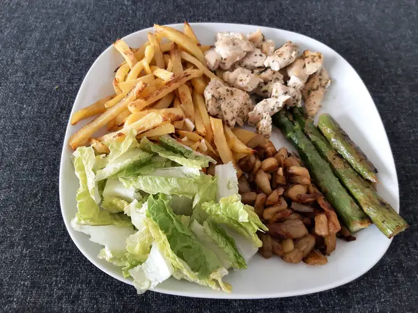 Homemade grilled chicken with french fries, asparagus, grilled chopped eggplant and green salad, served on a white plate