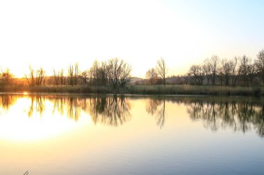 Sonbahar ağaçları göl boyunca altın ve kırmızı renkler sergilerler, sakin yansıtıcı suda güzel yansıtılır..