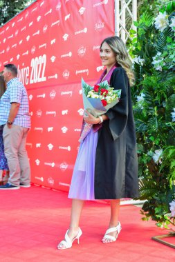 TIMISOARA, ROMANIA - 12 Temmuz 2022: Akademik kıyafetiyle gülümseyen genç bir kadın başarı ve umut dolu yeni başlangıçların anılarını yakalıyor