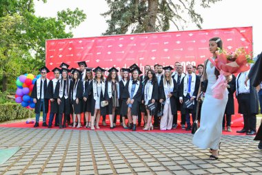 TIMISOARA, ROMANIA - 12 Temmuz 2022: Mutlu öğrenciler üniversite mezuniyetlerini arkadaşlarıyla ve aileleriyle birlikte kutlayan hatırlanmaya değer fotoğraflar için poz veriyorlar.