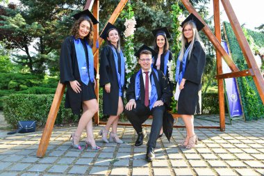 TIMISOARA, ROMANIA - 12 Temmuz 2022: Mutlu öğrenciler üniversite mezuniyetlerini arkadaşlarıyla ve aileleriyle birlikte kutlayan hatırlanmaya değer fotoğraflar için poz veriyorlar.
