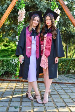TIMISOARA, ROMANIA - 12 Temmuz 2022: İki genç kadın başarılarını kutlamak için mezuniyet töreninde mutlu poz verdiler
