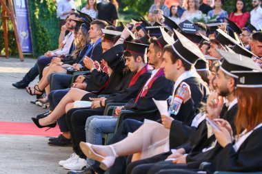 TIMISOARA, ROMANIA - 12 Temmuz 2022: Mezuniyet törenleri sırasında profesörlerin konuşmalarını dikkatle dinleyen koltuklarda oturan mezunlar