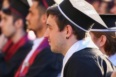 TIMISOARA, ROMANIA - 12 Temmuz 2022: Mezuniyet törenleri sırasında profesörlerin konuşmalarını dikkatle dinleyen koltuklarda oturan mezunlar