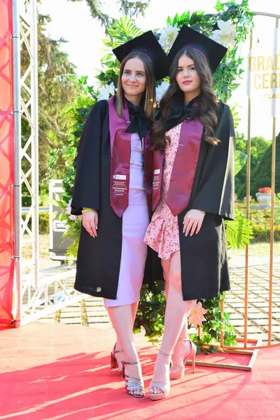 TIMISOARA, ROMANIA - 12 Temmuz 2022: İki genç kadın başarılarını kutlamak için mezuniyet töreninde mutlu poz verdiler