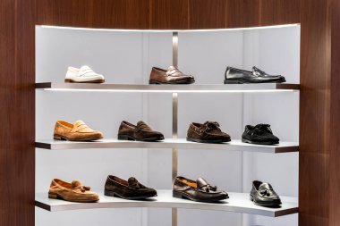 Elbise ve aksesuar dükkanında raflar. Raflarda şık erkek ayakkabıları var. Bir sürü klasik ayakkabı ve bot. Kahverengi tonlama. Mağazada güzel deri adam ayakkabıları sergileniyor.