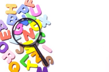 English alphabet made of square wooden tiles with the English alphabet scattered on white background. The concept of thinking development, grammar. Magnifier placed on English letters