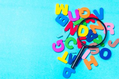 English alphabet made of square wooden tiles with the English alphabet scattered on blue background. The concept of thinking development, grammar. Magnifier placed on English letters