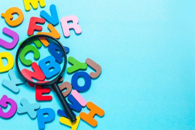 English alphabet made of square wooden tiles with the English alphabet scattered on blue background. The concept of thinking development, grammar. Magnifier placed on English letters
