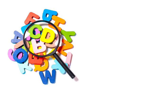 English alphabet made of square wooden tiles with the English alphabet scattered on white background. The concept of thinking development, grammar. Magnifier placed on English letters