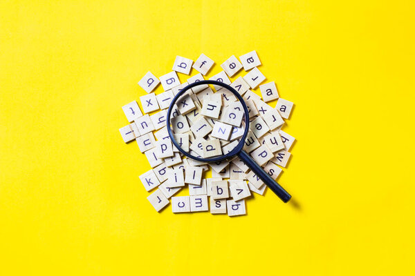 English alphabet made of square wooden tiles with the English alphabet scattered on yell0w background. The concept of thinking development, grammar. Magnifier placed on English letters